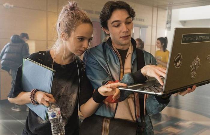 Jane et Simon dans la série Qui ment?, en train de regarder un ordinateur portable debout au milieu d'un couloir du lycée. Roman young adult résumé spoilant